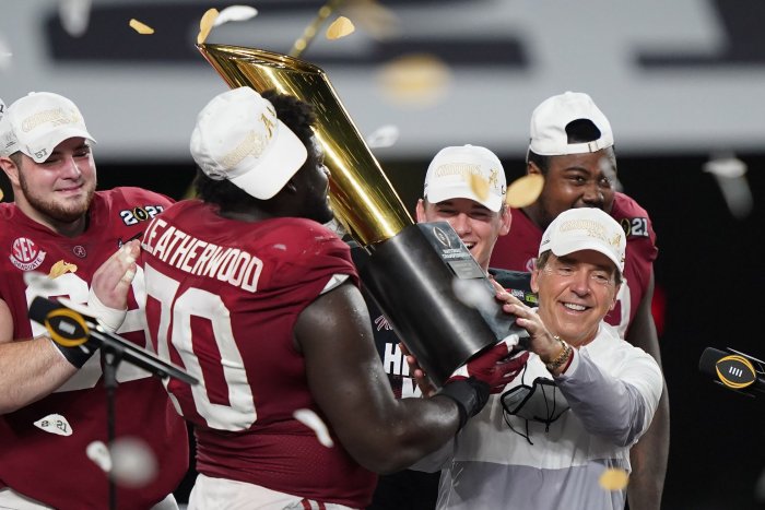 Coach Nick Saban gets help hoisting the 2020 National Championship trophy. 