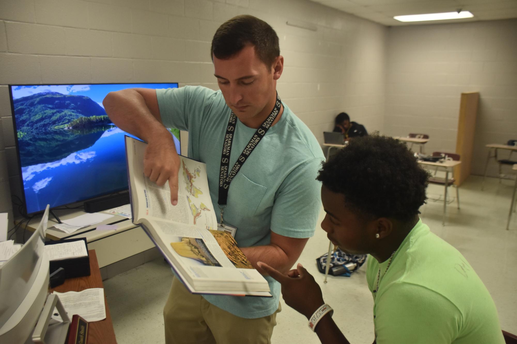 Showing a student where to find a passage in the text, coach Spencer Smith displays his passion for teaching. Smith, also seen on the sidelines on Friday nights, said he often thinks of the why of being in the classroom.