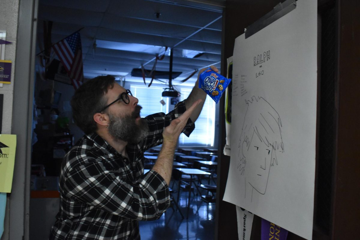 Public speaking teacher, Evan Carter demonstrates a demo speech enthusiastically with a bag of Chips Ahoy.  